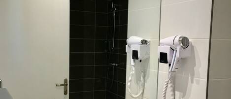 Un baño moderno con un lavabo blanco, un secador de pelo portátil y un espejo que refleja la zona de la ducha.