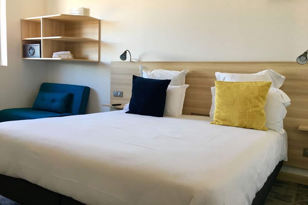 Una habitación de hotel con una cama grande, mesitas de noche, una lámpara y una silla azul.