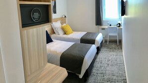Habitación de hotel con dos camas, un escritorio, una silla, un televisor y un ventanal con cortinas.