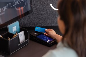 A person using a mobile device at a self-service kiosk with a QR code and a card reader. - Hey Lou Hotel Frankfurt Airport (Kelsterbach)