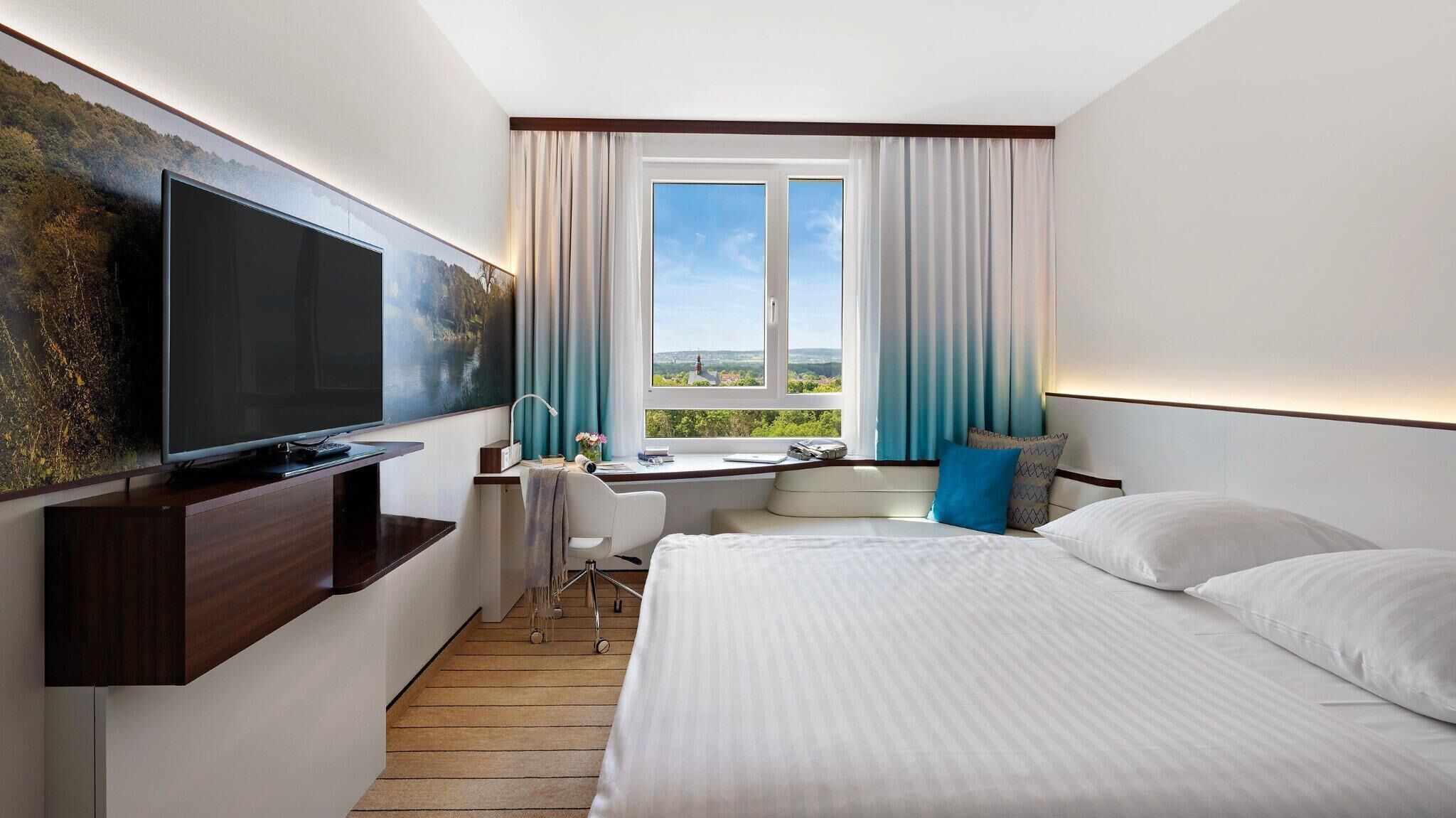 Een hotelkamer met een bed, een bureau, een televisie en een raam met gordijnen.