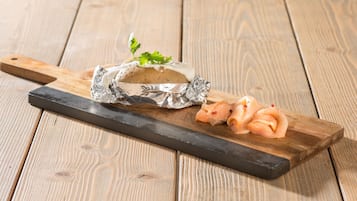 A wooden cutting board with a piece of food wrapped in foil and sliced food on a wooden surface.