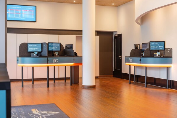 A reception area with two desks, a digital flight information board, and a wooden floor. - Hey Lou Hotel Frankfurt Airport (Kelsterbach)