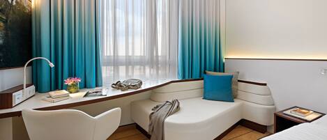A hotel room with a desk, a chair, a bed, and a window with curtains.