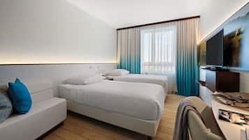 A hotel room with two beds, a sofa, a TV, and a desk with a chair.