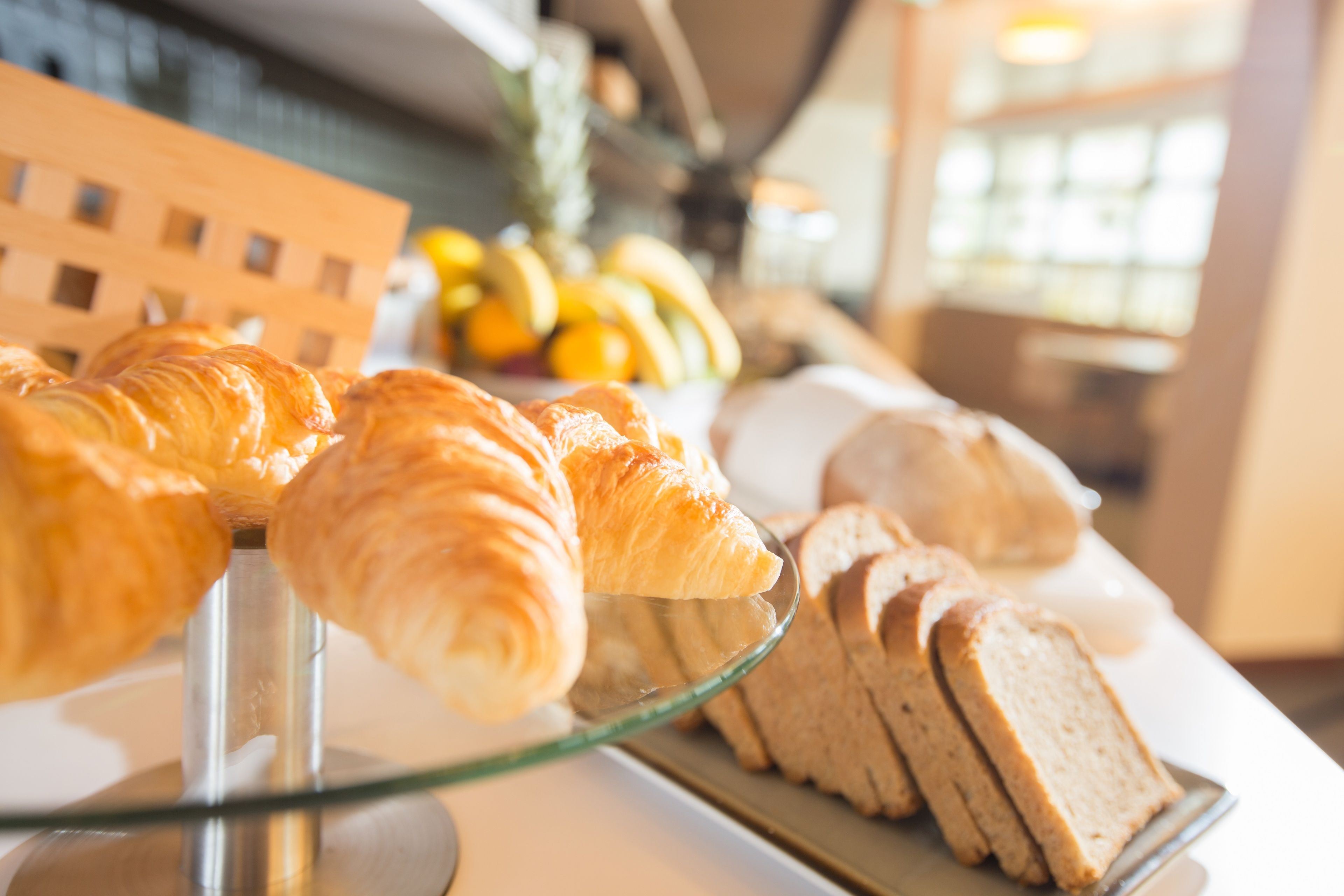 A display of pastries and bread on a glass stand in a bakery.