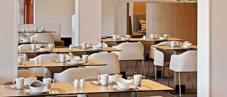A modern dining area with multiple tables and chairs, yellow pendant lights, and a clean, minimalist design.