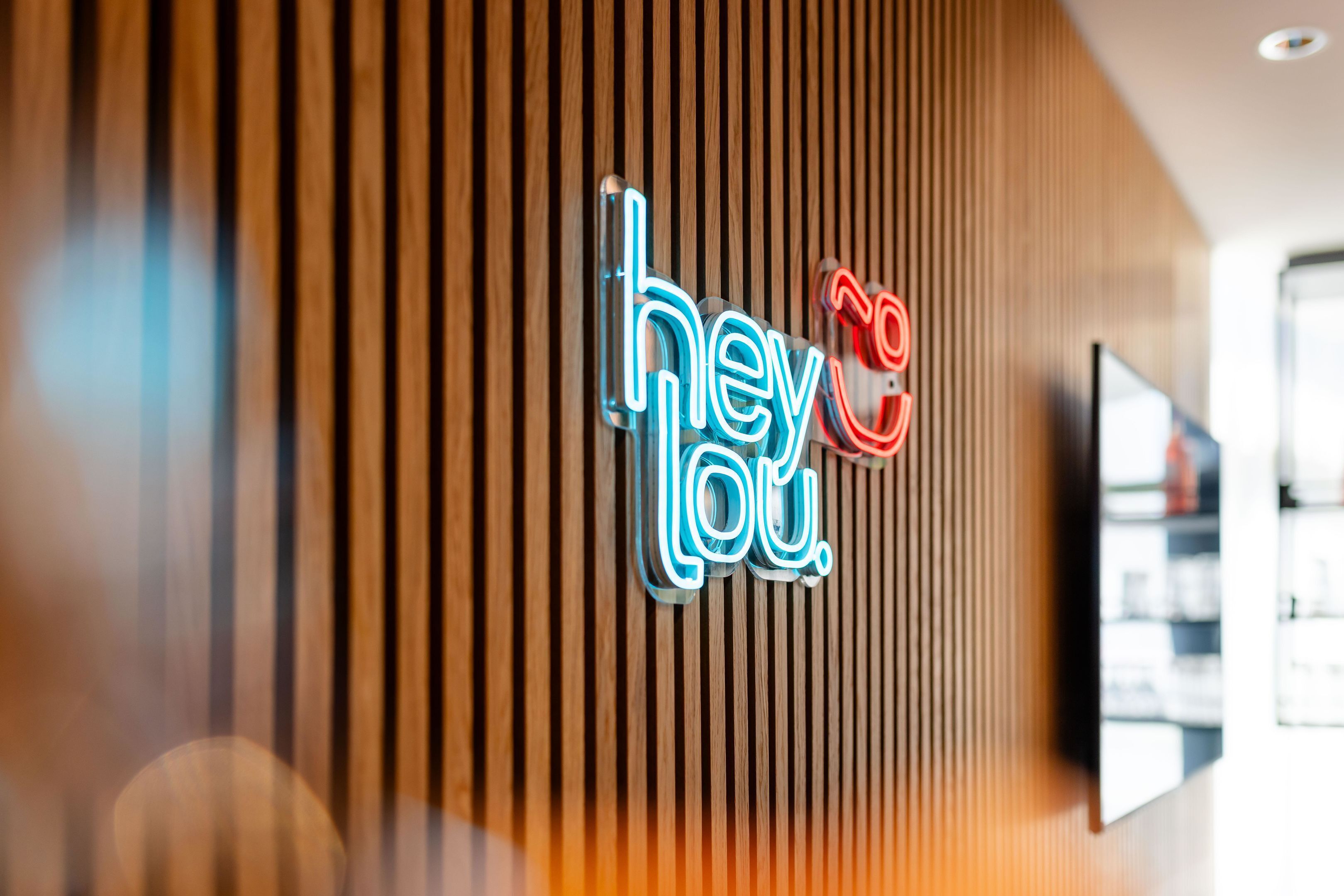 A neon sign with the text 'hey you' on a wooden wall.
