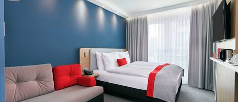 A hotel room with a bed, a sofa, a TV, and a window with curtains.