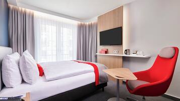 Hotellihuone, jossa on sänky, työpöytä, tuoli, televisio ja ikkuna, jossa on verhot.