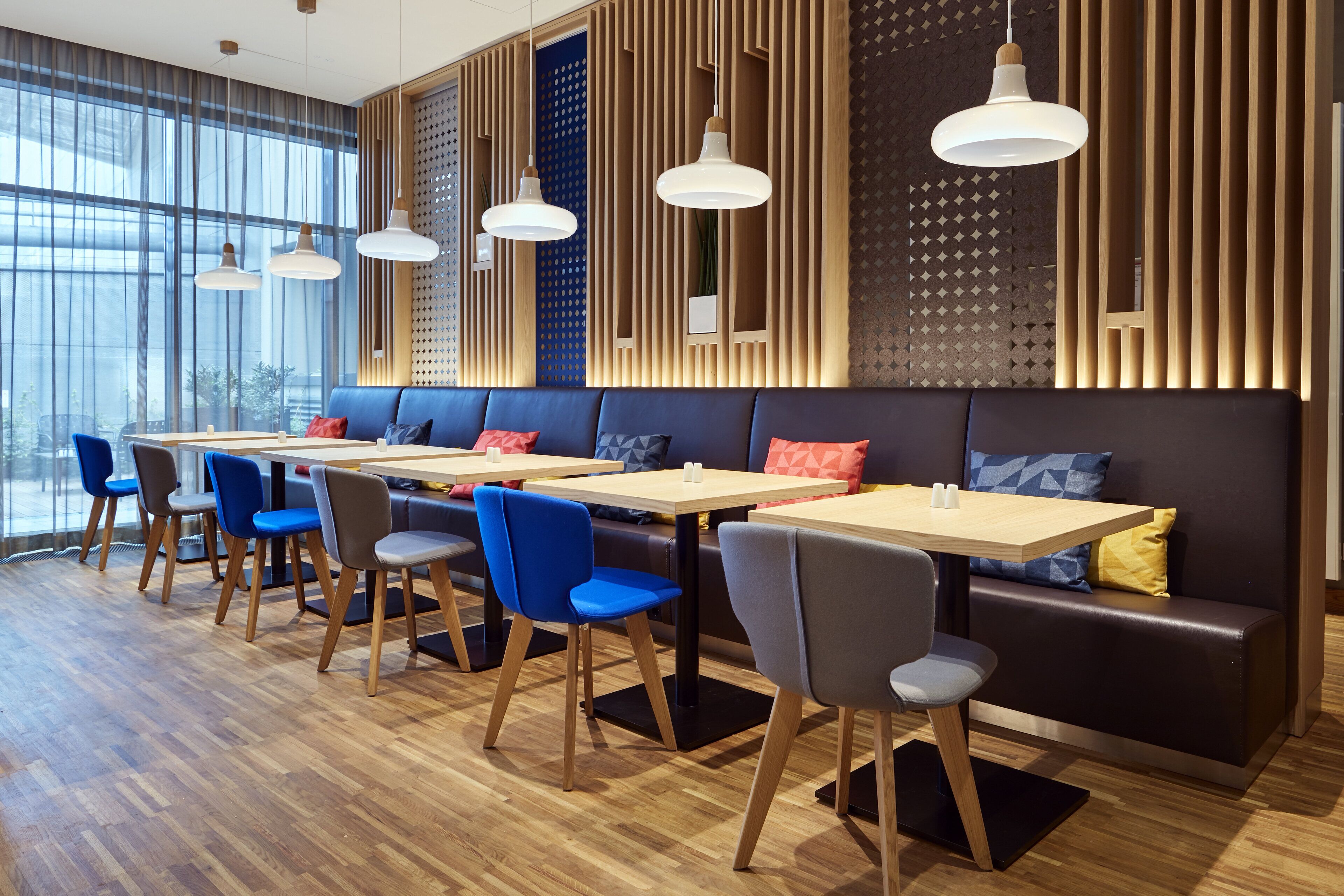 Un restaurante moderno con suelo de madera, sillas azules y grises, y una larga barra con mesas.