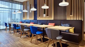 A modern restaurant with wooden flooring, blue and gray chairs, and a long counter with tables.