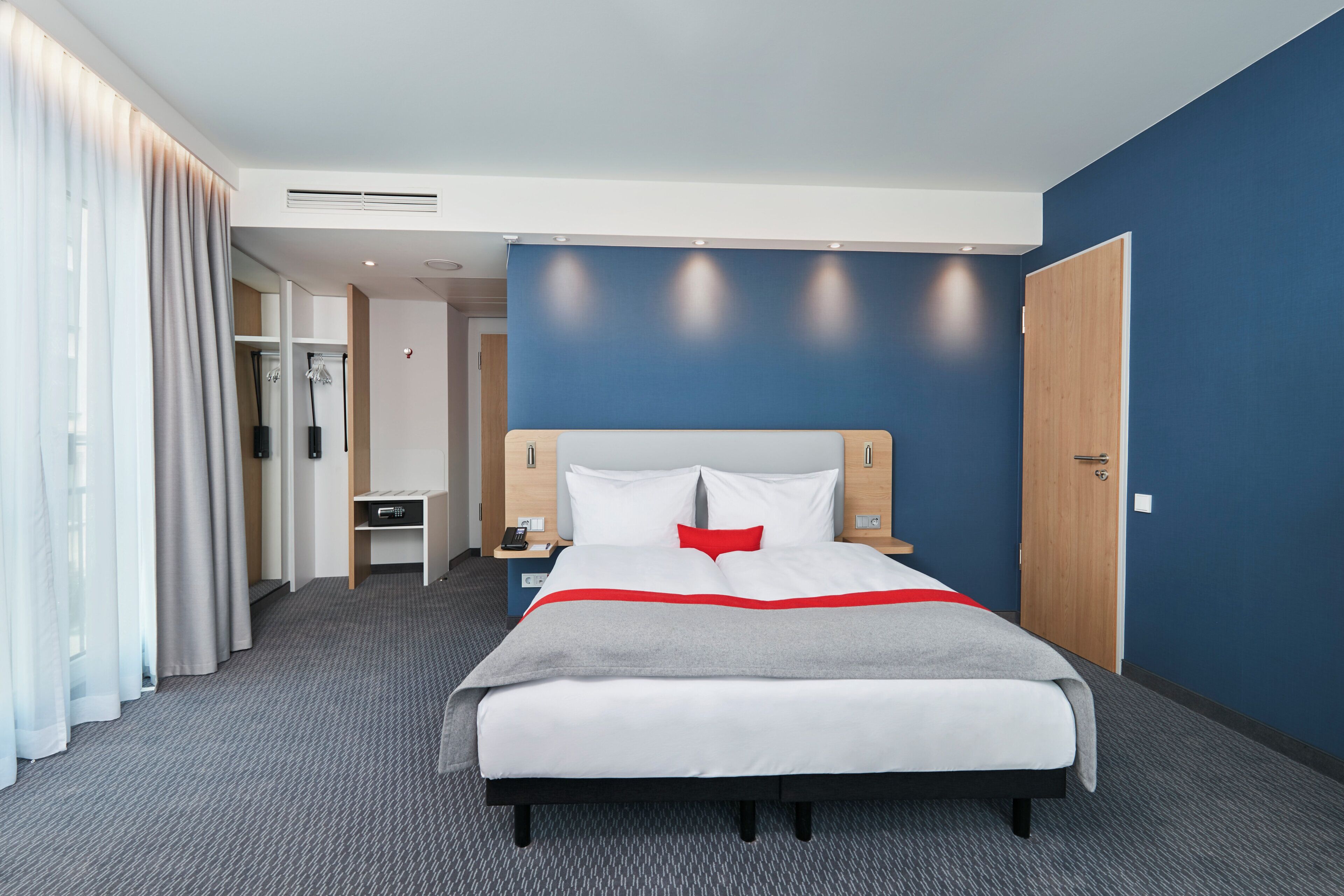 A hotel room with a bed, bedside tables, a desk, and a wardrobe.