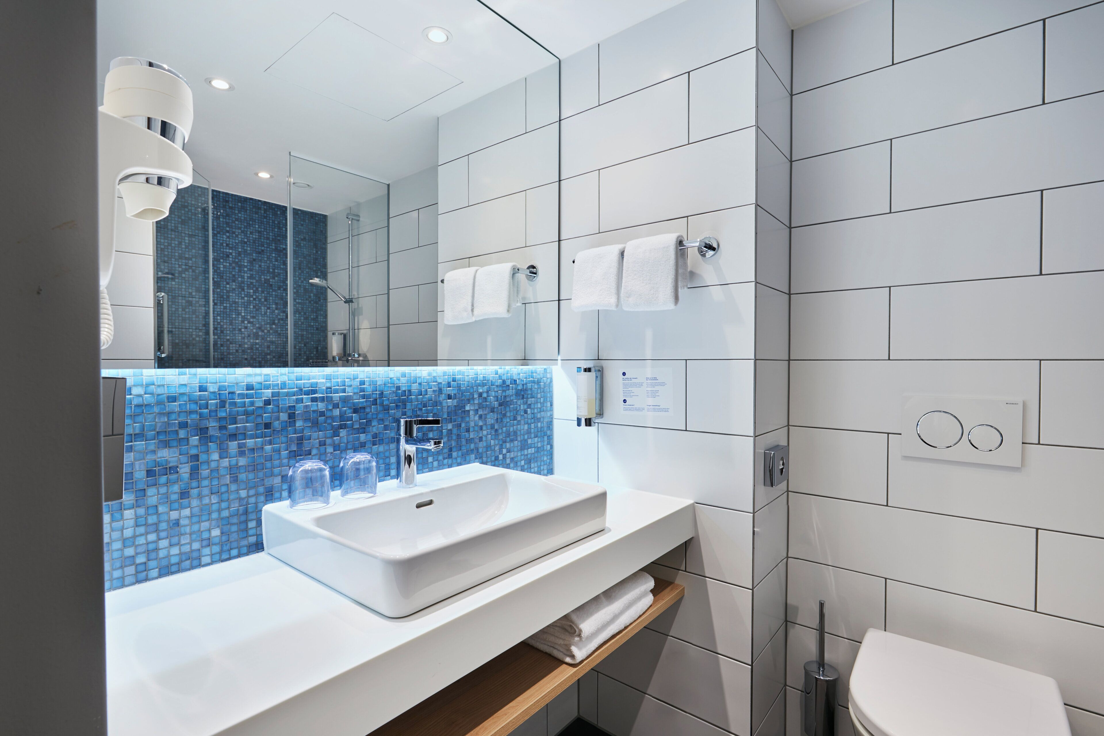 A modern bathroom with a white sink, a glass shower enclosure, and a toilet.