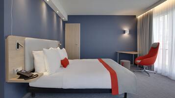 Ein modernes Hotelzimmer mit einem großen Bett, einem Schreibtisch, einem Stuhl und einem Telefon auf dem Nachttisch.