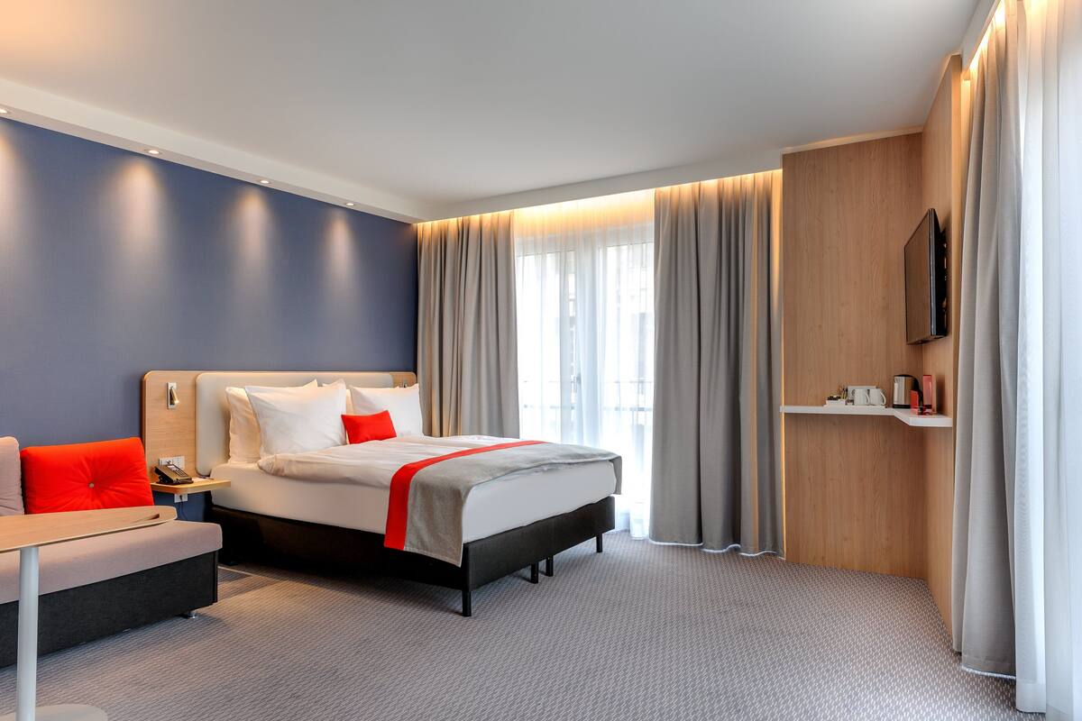 A modern hotel room with a bed, bedside table, and a television mounted on the wall.