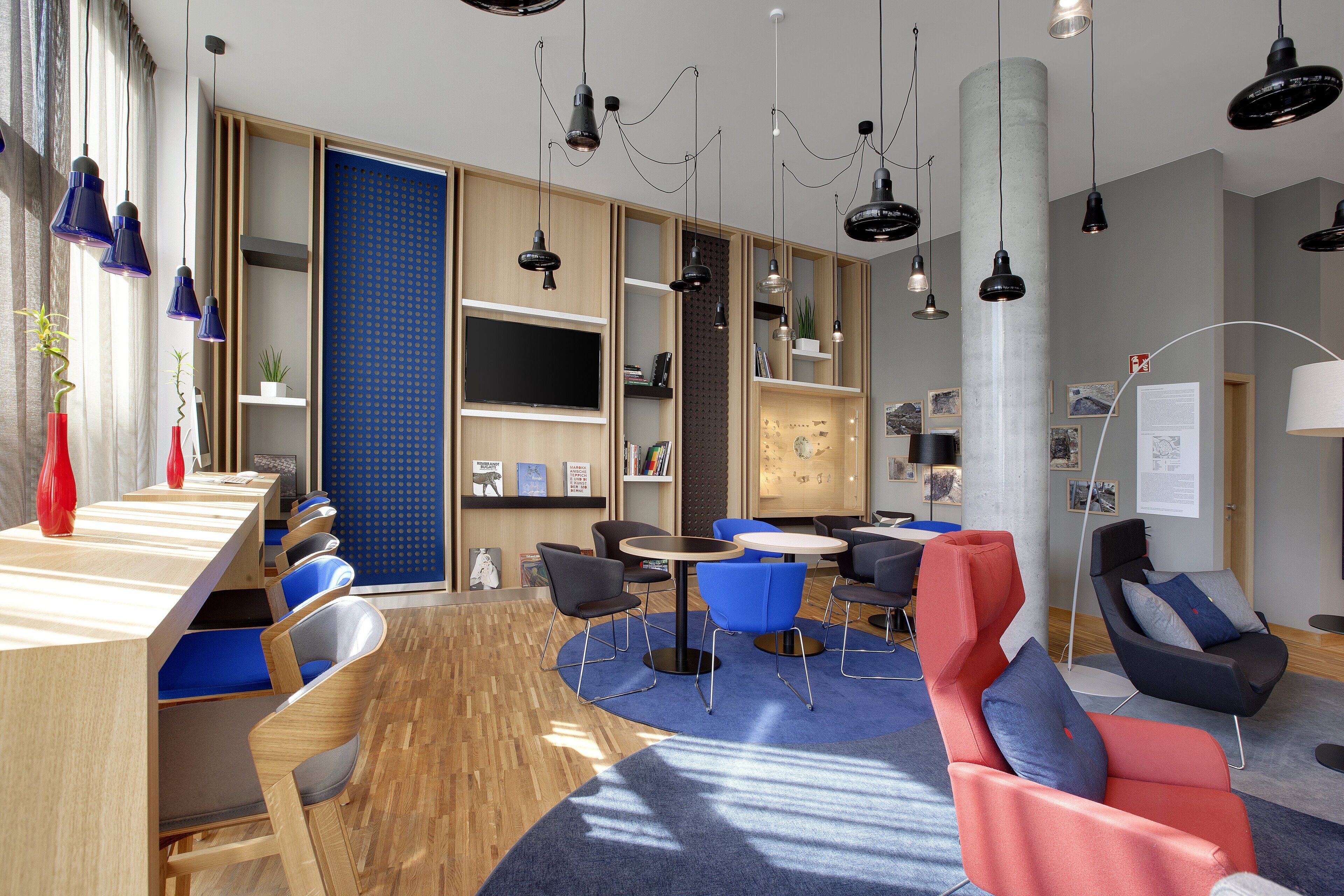 A modern lounge area with wooden tables, blue and red chairs, and a large blue carpet.