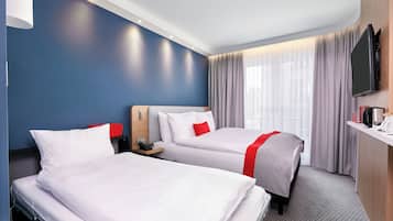 Habitación de hotel con dos camas, un escritorio, un televisor y un ventanal con cortinas.