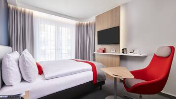 Una habitación de hotel moderna con una cama, una silla roja, una mesita, un televisor y una cafetera.