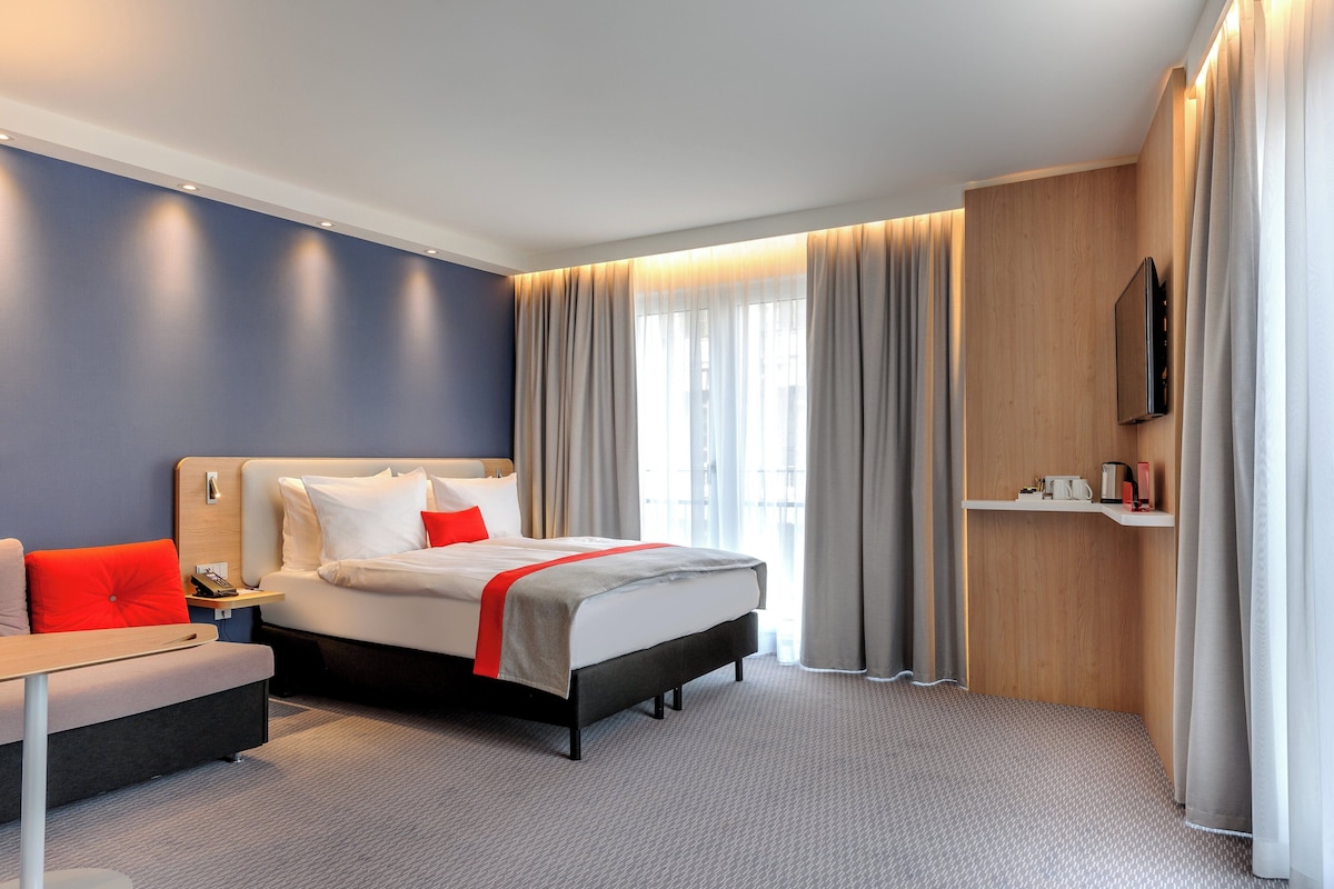 Ein modernes Hotelzimmer mit einem Bett, Nachttisch und einem an der Wand befestigten Fernseher.