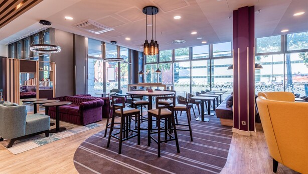 Zona lounge moderna con un tavolo rotondo, sgabelli da bar, divani e un'ampia finestra con vista sull'esterno.