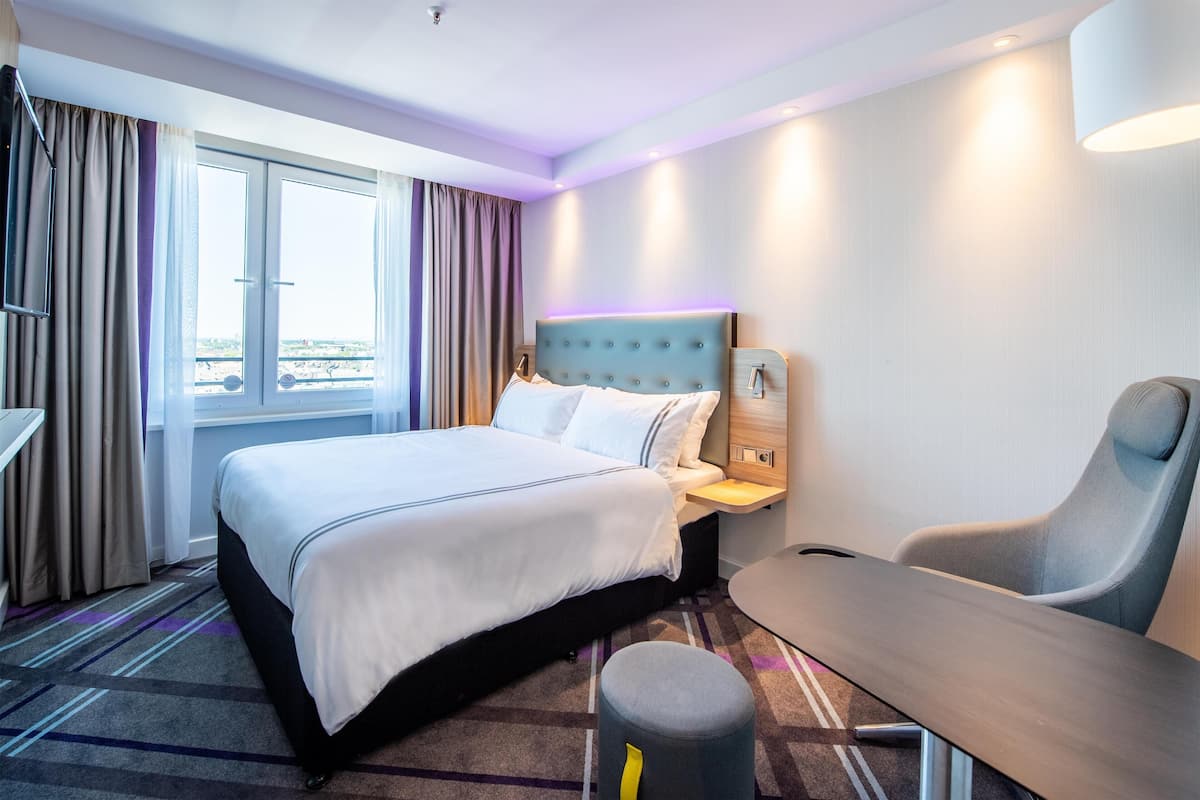 A hotel room with a bed, a desk, a chair, and a window with curtains.