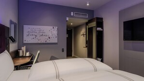 Una camera d'albergo moderna con un letto grande, una scrivania con una sedia, una TV a schermo piatto e un pannello decorativo al muro.