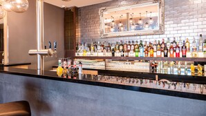 Zona bar con diverse bottiglie di liquori, uno specchio e lampade a sospensione.