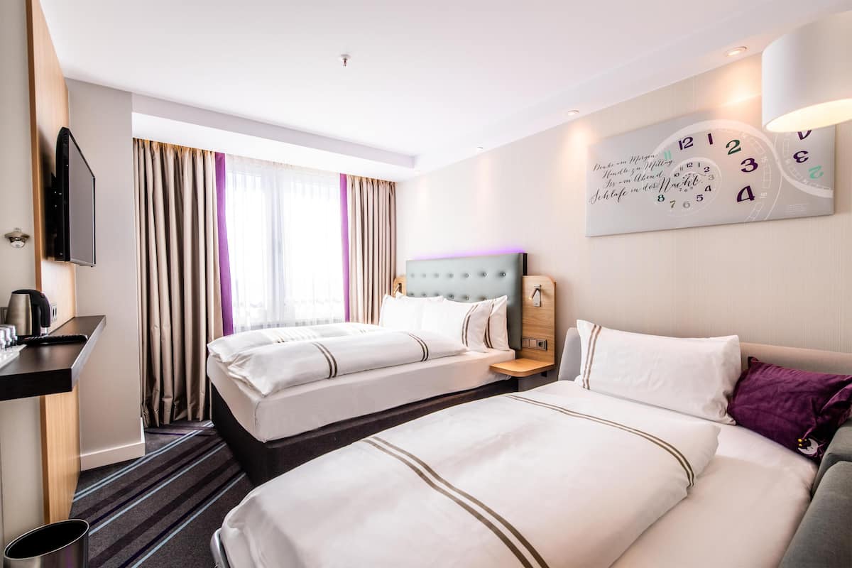 A hotel room with two beds, a TV, a clock, and a window with curtains.