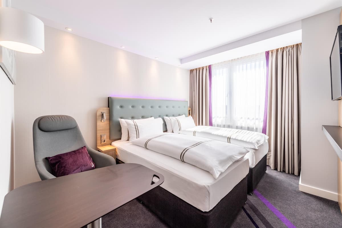 A hotel room with a bed, a desk, a chair, a TV, and a window with curtains.