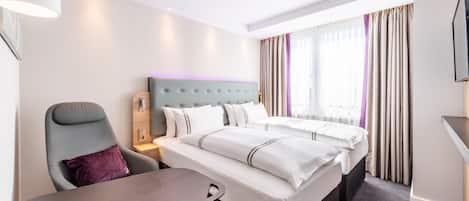 Habitación de hotel con cama, escritorio, silla, televisor y ventana con cortinas.
