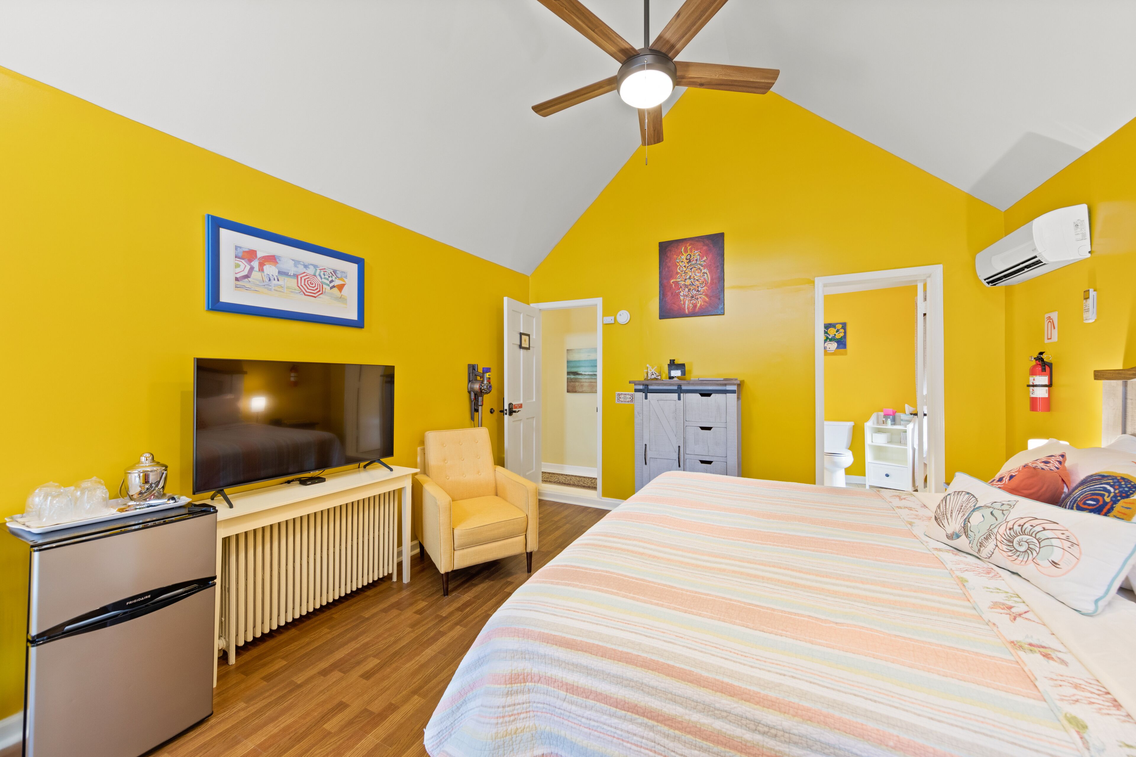 A bedroom with a bed, a ceiling fan, a TV, a refrigerator, a chair, and a wardrobe.