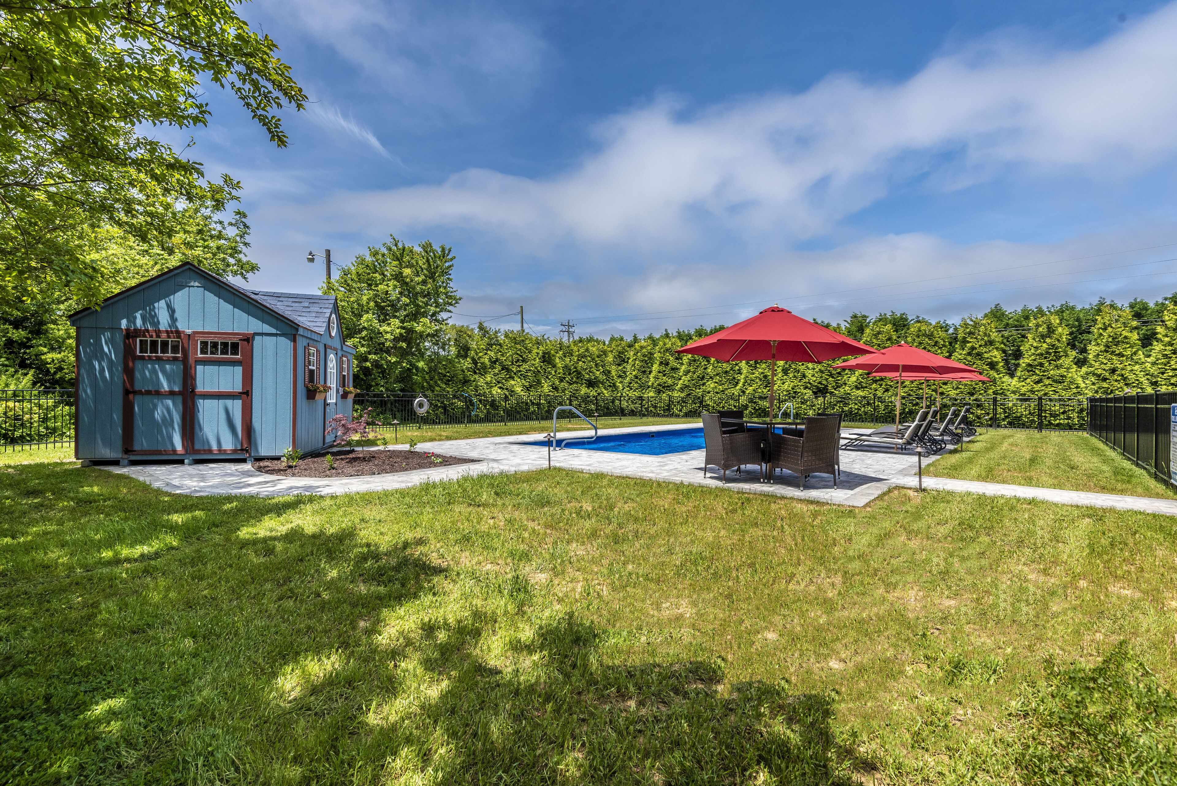 A backyard with a pool, a small shed, and a patio area with red umbrellas.