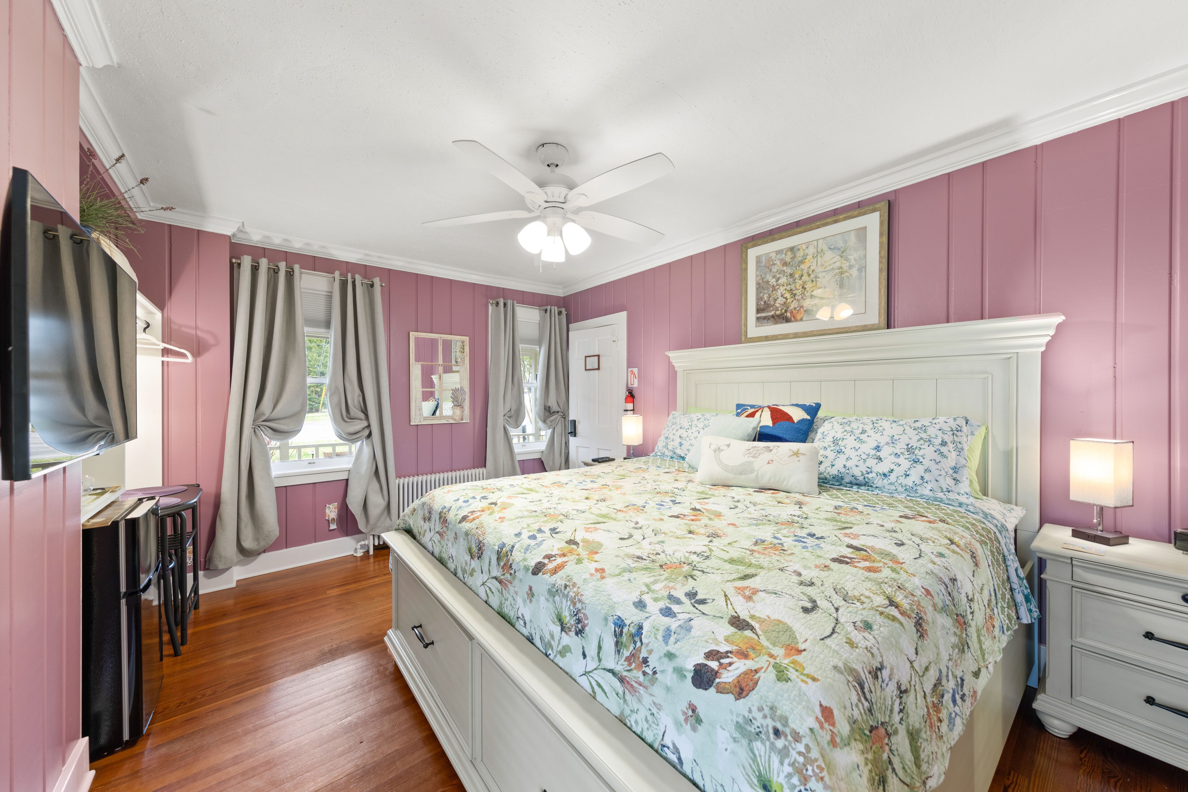 A bedroom with a bed, a nightstand, a dresser, a ceiling fan, and a window with curtains.