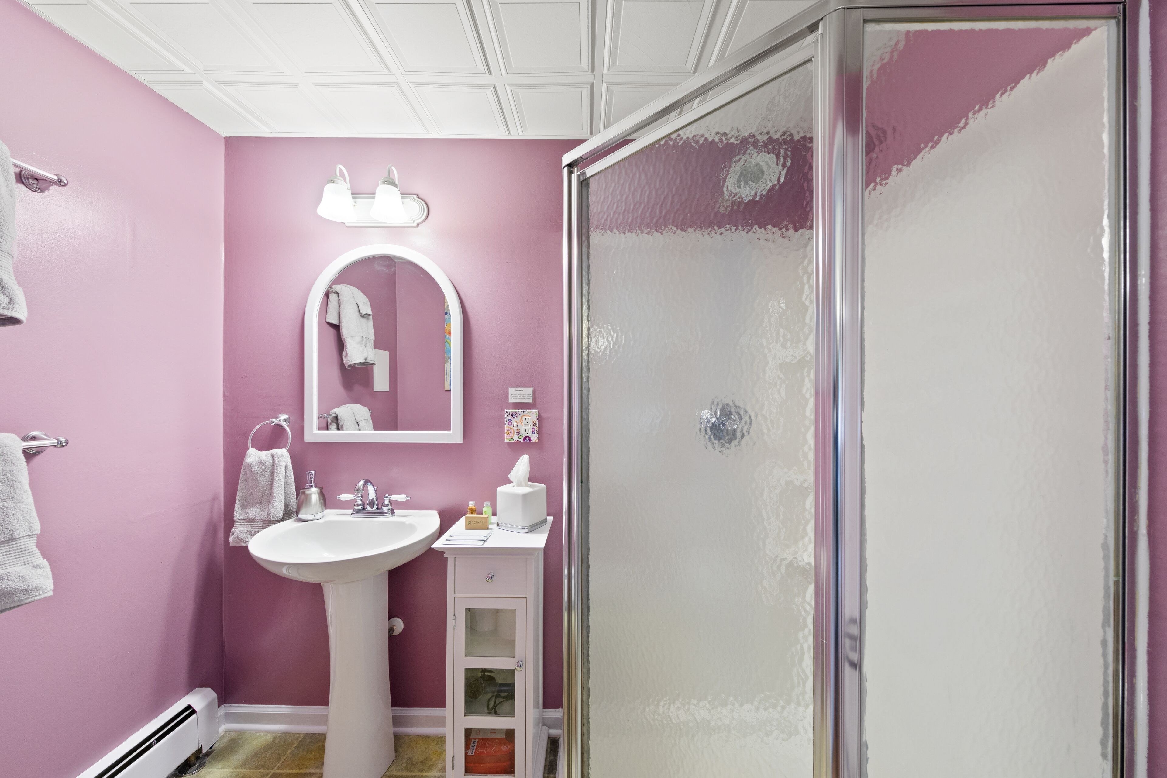 A bathroom with a pink wall, a white sink, a mirror, and a glass shower enclosure.