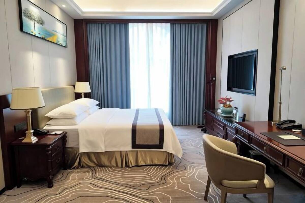 A hotel room with a large bed, a desk, a chair, a TV, and a window with curtains.