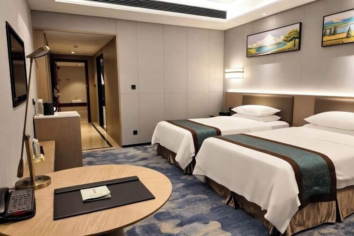 A hotel room with two beds, a desk, a chair, a telephone, and a small table with a menu.