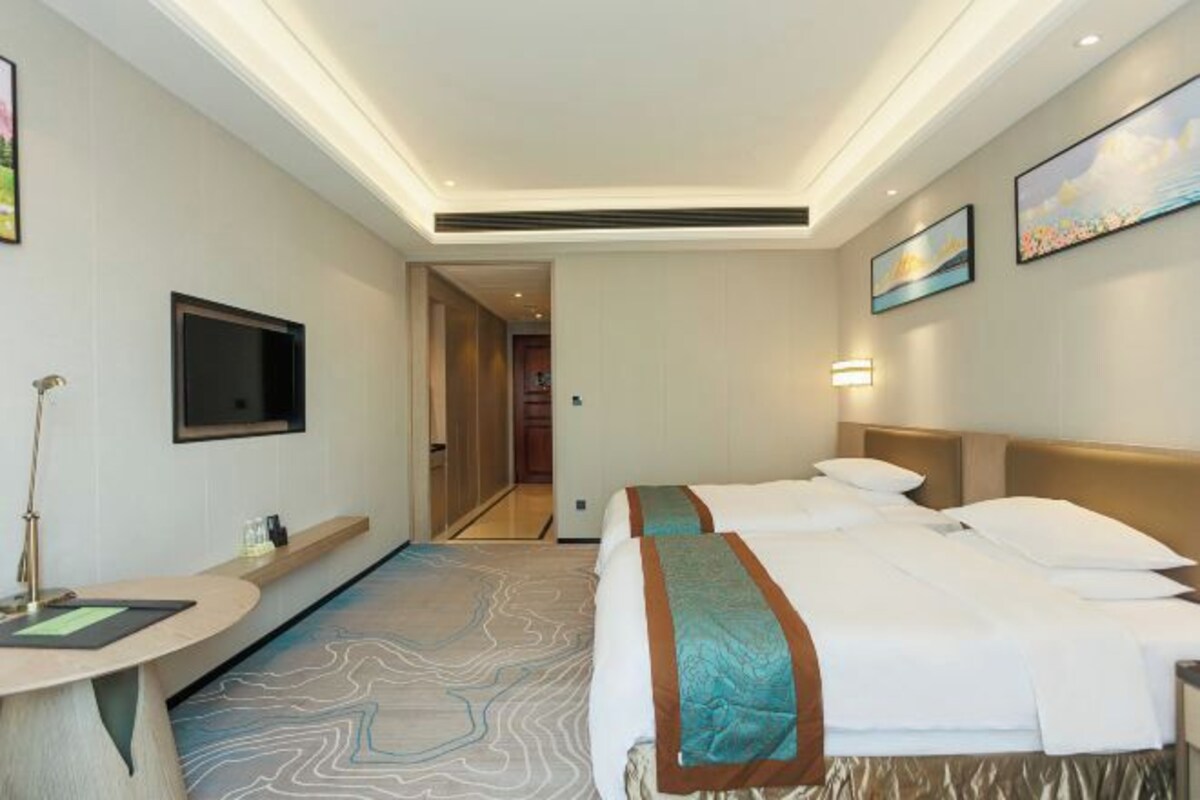 A hotel room with a bed, a desk, a TV, and a hallway leading to another room.