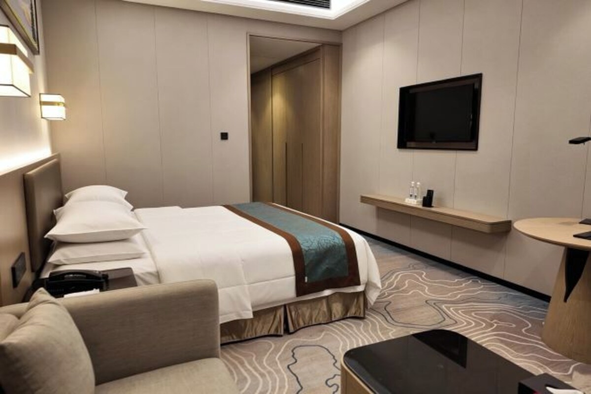 A hotel room with a bed, a sofa, a TV, a small table, and a bathroom area.