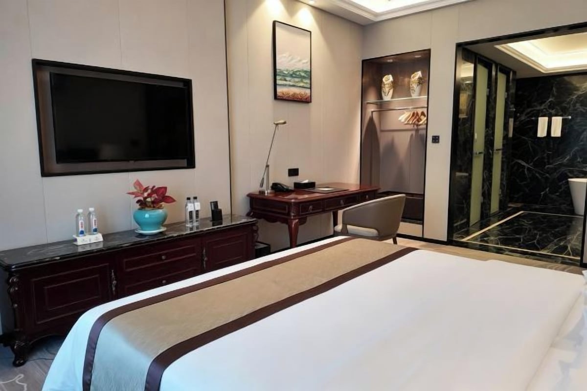 Une chambre d’hôtel avec un grand lit, un bureau avec une chaise, un téléviseur à écran plat, un miroir et une vue sur l’extérieur.
