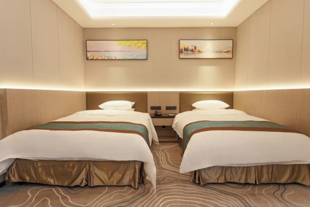 A hotel room with two beds, a skylight, and two wall-mounted paintings.