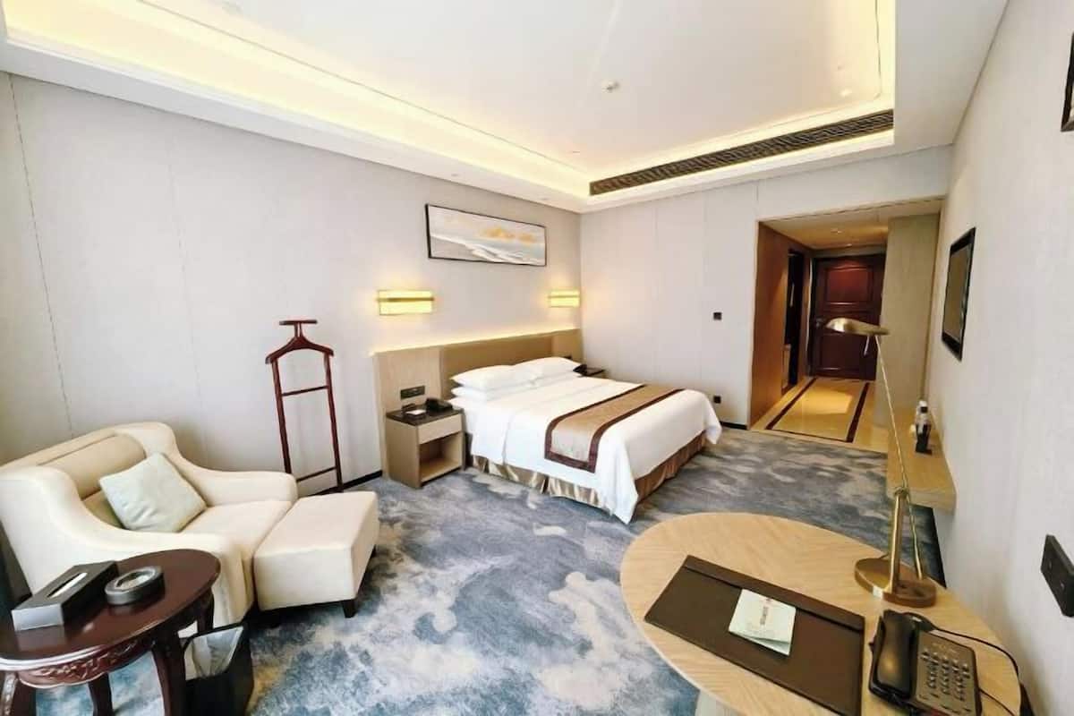 A hotel room with a bed, a sofa, a desk, a lamp, and a bedside table.