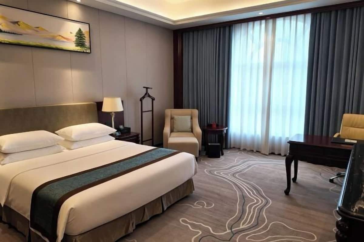 A hotel room with a large bed, a desk, a chair, a lamp, and a painting on the wall.