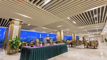 A spacious indoor area with a long table set for dining, surrounded by chairs, and a modern ceiling design.