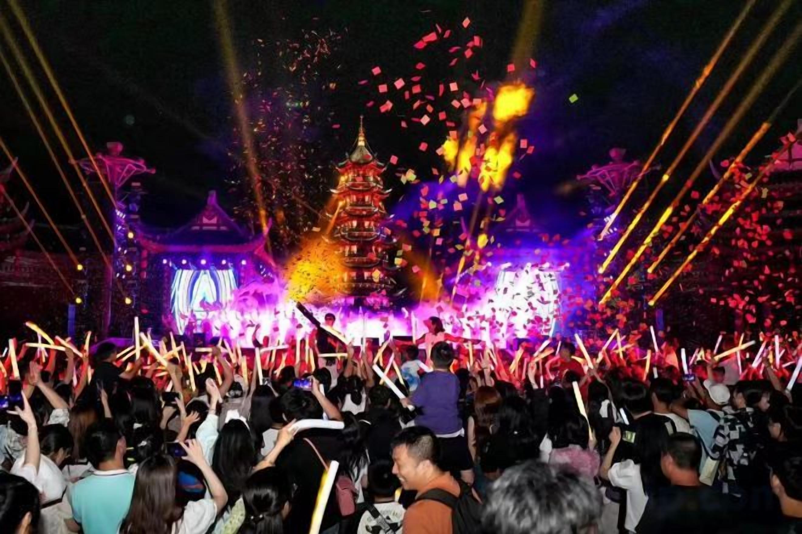 A crowd of people at an event with a large illuminated pagoda in the background.
