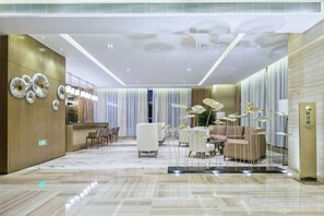 Een hotellobby met een receptiebalie, een zithoek en een moderne kroonluchter.