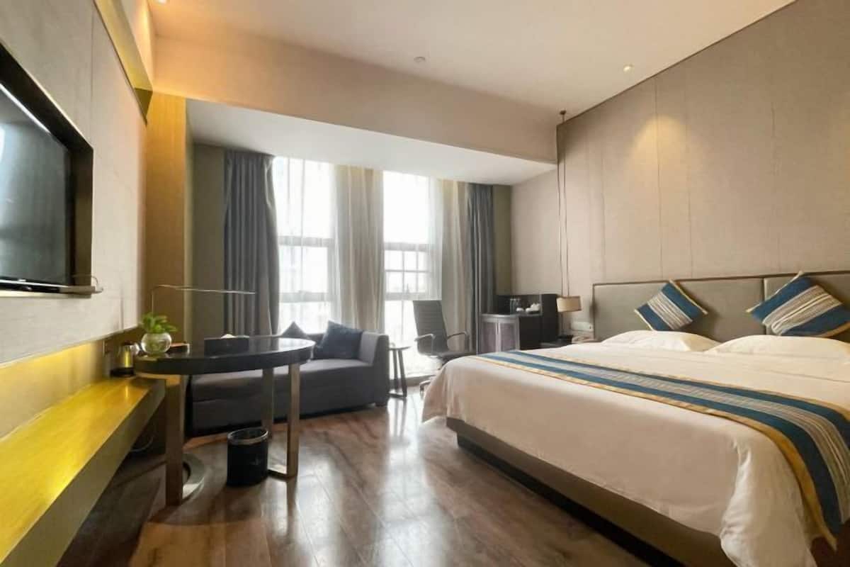 A modern hotel room with a large bed, a desk, a chair, and a TV.