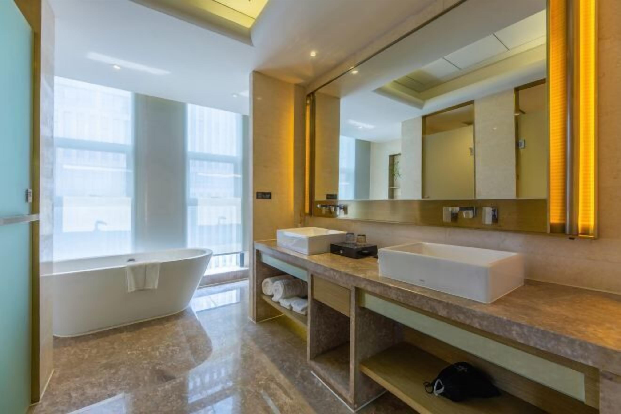 Een moderne badkamer met een vrijstaand bad, twee wastafels, een grote spiegel en een badmeubel met planken.