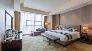 Een hotelkamer met een groot bed, een bankje, een bureau en een raam met gordijnen.