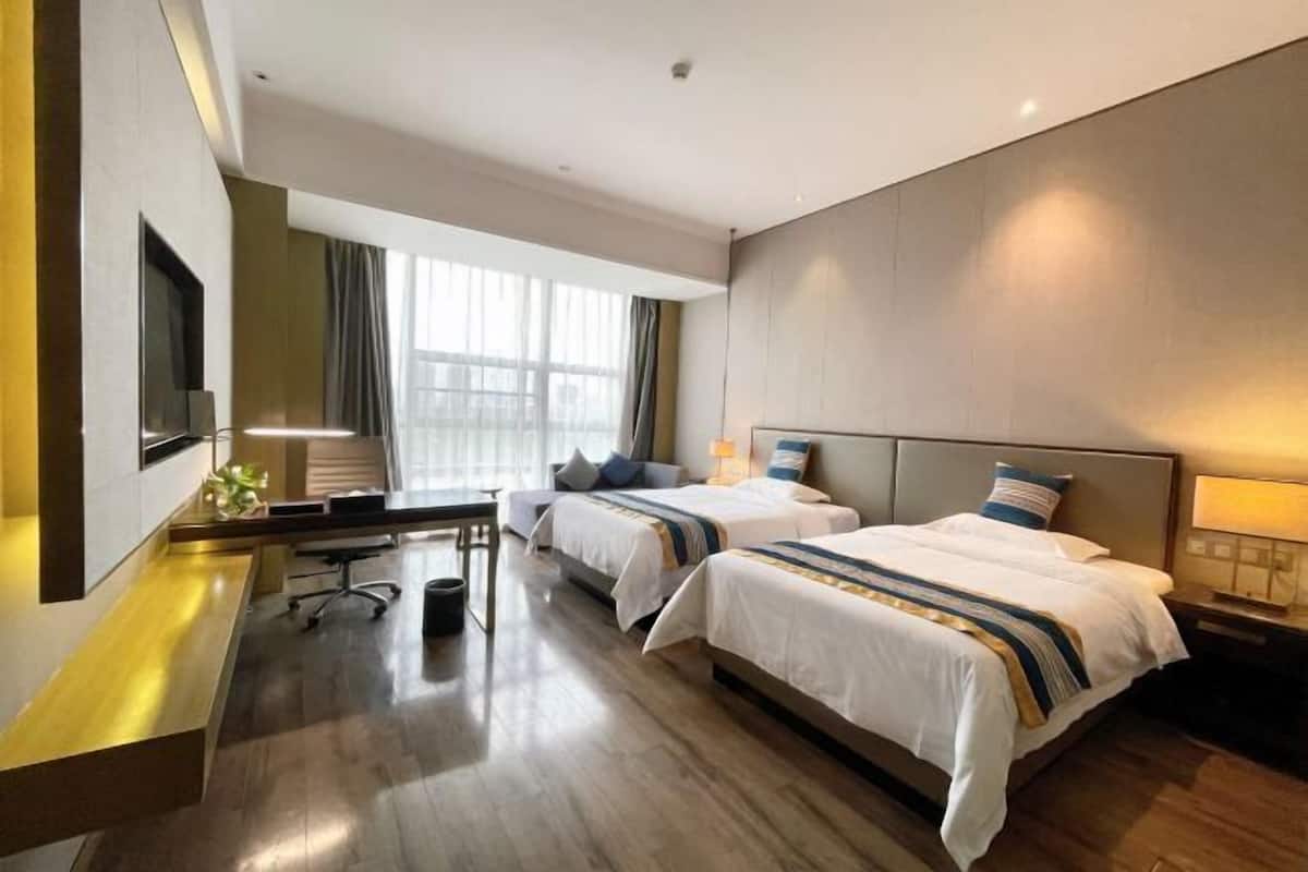 A hotel room with two beds, a desk, a chair, a TV, and a window with curtains.